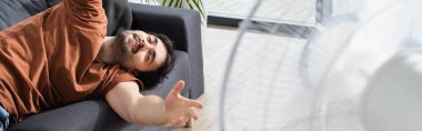 Bulanık elektrikli yelpaze ve pankartın yanındaki kanepede yatan memnun genç adam.