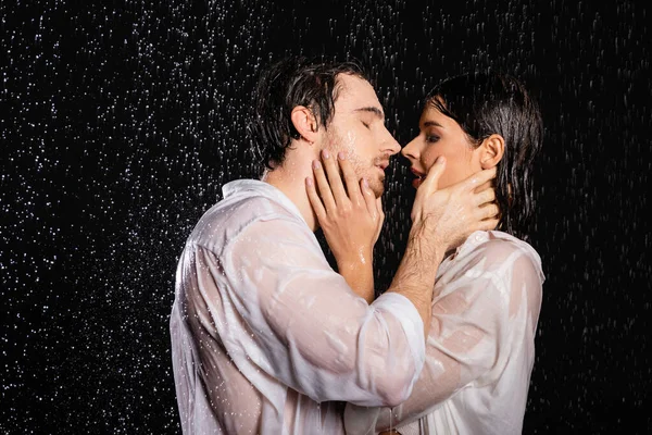 passionate sexy couple in wet clothes standing in rain drops on black background