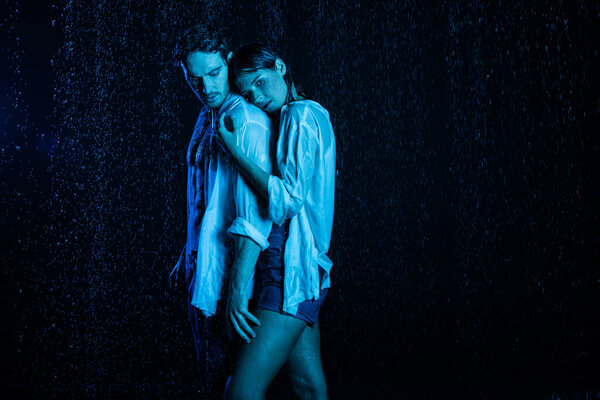 wet romantic couple gently hugging in water drops on black background with blue color filter 