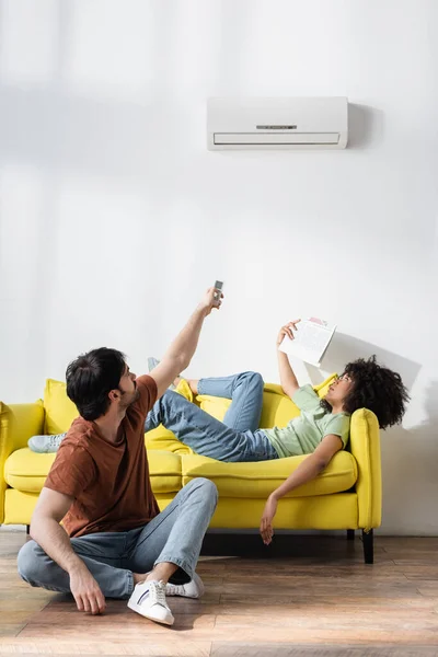 Man Met Afstandsbediening Buurt Van Airconditioner Afrikaanse Amerikaanse Vriendin Zwaaien — Stockfoto