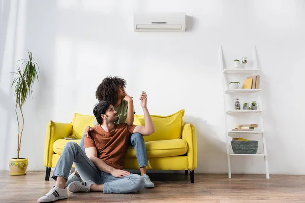 Displeased Interracial Couple Looking Air Conditioner While Sitting Sofa — Stock Photo, Image