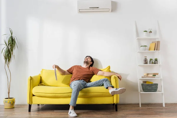 Homem Segurando Jornal Enquanto Deitado Sofá Amarelo Sofrendo Calor Sala — Fotografia de Stock