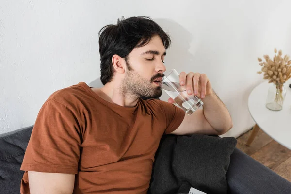 bearded man drinking water while suffering from heat