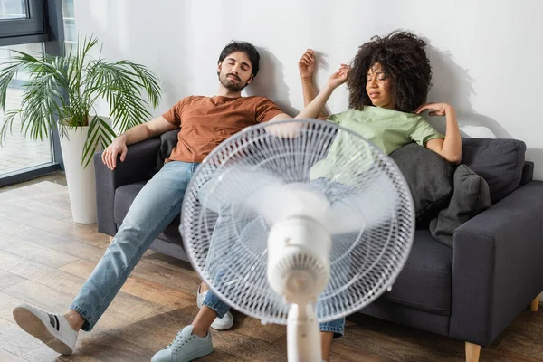 Erschöpftes Gemischtrassiges Paar Sitzt Auf Couch Neben Verschwommenem Elektroventilator Wohnzimmer — Stockfoto