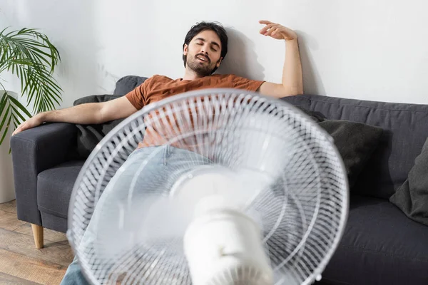 Hombre Barbudo Contento Sentado Sofá Cerca Ventilador Eléctrico Borroso —  Fotos de Stock