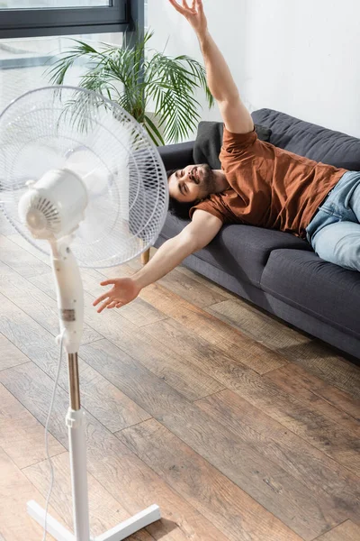 Glad Ung Man Ligger Soffan Nära Suddig Elektrisk Fläkt — Stockfoto