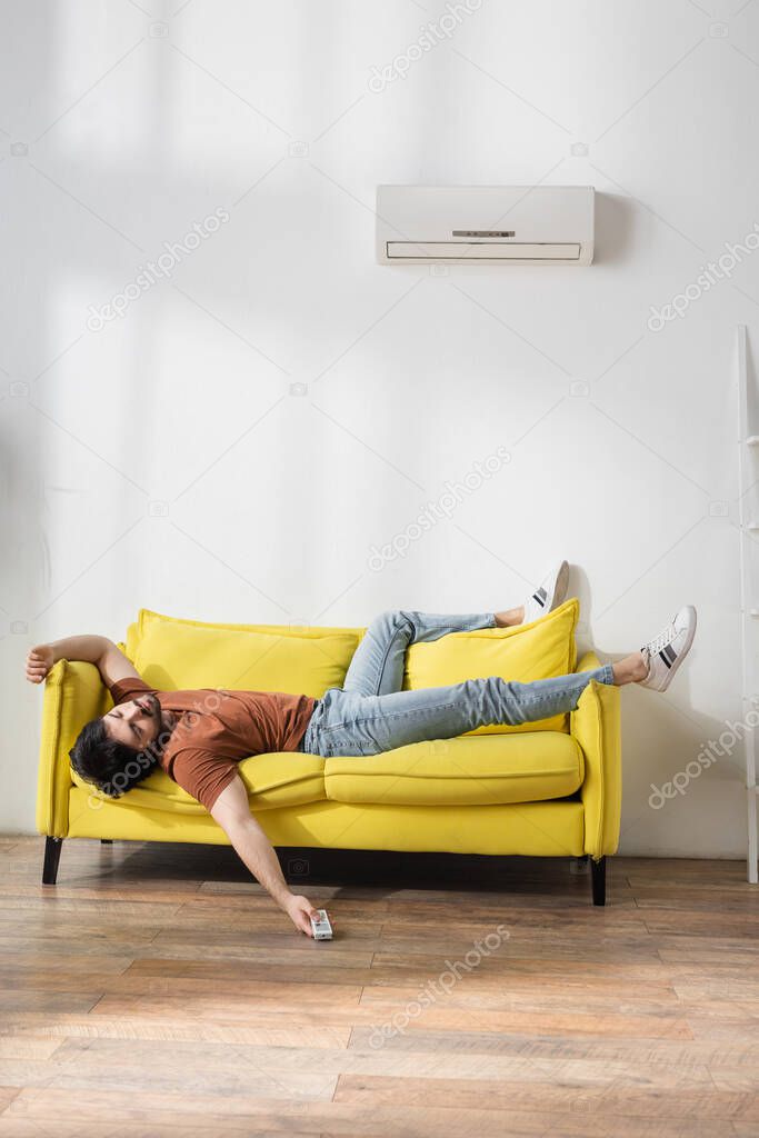 man holding remote controller while lying on couch and suffering from heat in living room
