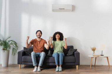 Modern oturma odasındaki koltukta otururken mutlu çoklu etnik coşku, hvac konsepti 