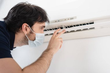 Klima yakınında jest yapan tıbbi maskeli bir tamirci. Klimayı kontrol ediyor.