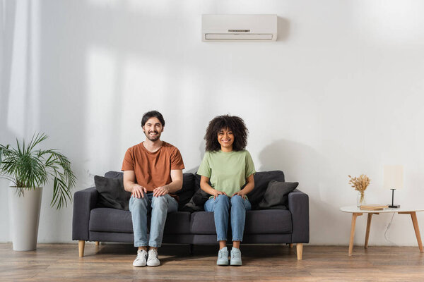 happy multiethnic sitting on sofa in modern living room, hvac concept 