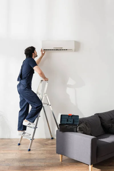 Bearded Handyman Overalls Standing Ladder While Fixing Broken Air Conditioner — Stock Photo, Image