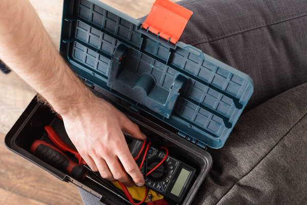 partial view of handyman taking digital multimeter from toolbox