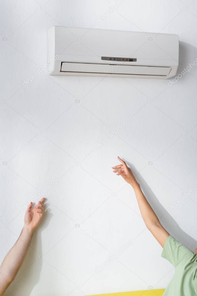 cropped view of multiethnic couple reaching air conditioner while suffering from heat in summer