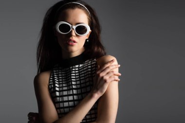 Saç bandı takmış zarif bir kadın ve gri üzerine izole edilmiş beyaz güneş gözlüğü takıyor.