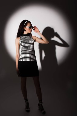 Moda modelinde tam uzunlukta ışıklandırma, güneş gözlüğünü ayarlama ve gri üzerinde poz verme 