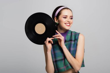 Saçbandı takmış neşeli bir kadın, gri renkte izole edilmiş retro vinil disk taşıyor.