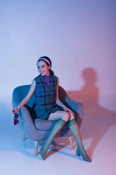 紫色の椅子に座りながらサングラスと雑誌を持っている笑顔の女性 — ストック写真