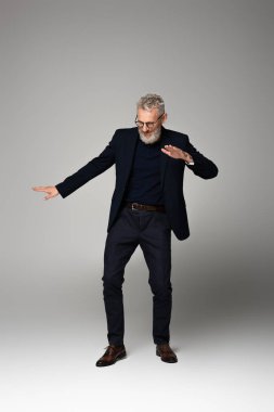 Uzun boylu, orta yaşlı, gözlüklü ve takım elbiseli, gri üzerinde dans eden adam.
