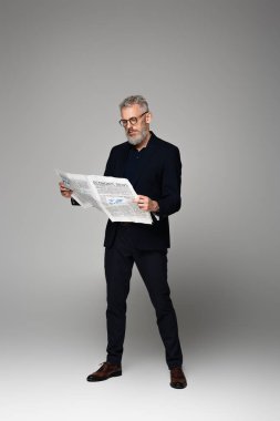 Gözlüklü ve takım elbiseli orta yaşlı bir adam Griler hakkında ekonomi haberleri okuyor.