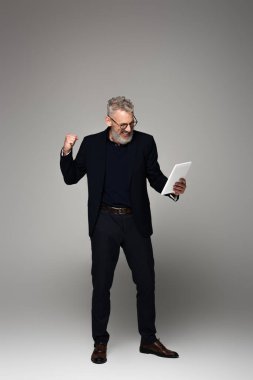 Gri saçlı, heyecanlı orta yaşlı işadamlarının dijital tablete bakıp, gri üzerine sevinçle bakmaları.