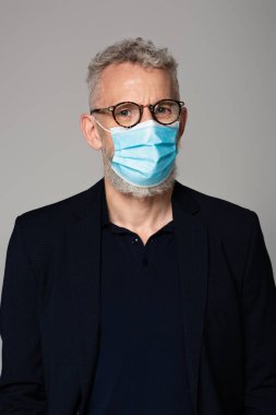 Gri saçlı, tıbbi maskeli olgun bir adam. Gri üzerinde izole edilmiş. 