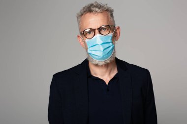 Gri saçlı, gözlüklü ve tıbbi maskeli orta yaşlı bir adam gri üzerine izole edilmiş. 