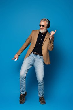 Uzun boylu, orta yaşlı, güneş gözlüklü, elinde akıllı telefon olan ve kulaklıkla müzik dinleyen bir adam.
