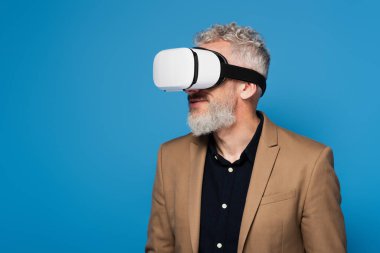 bearded middle aged man in vr headset isolated on blue  clipart