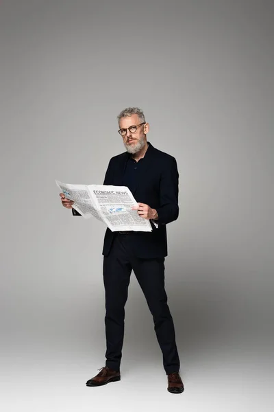 Mann Mittleren Alters Brille Und Anzug Mit Wirtschaftszeitung Auf Grau — Stockfoto
