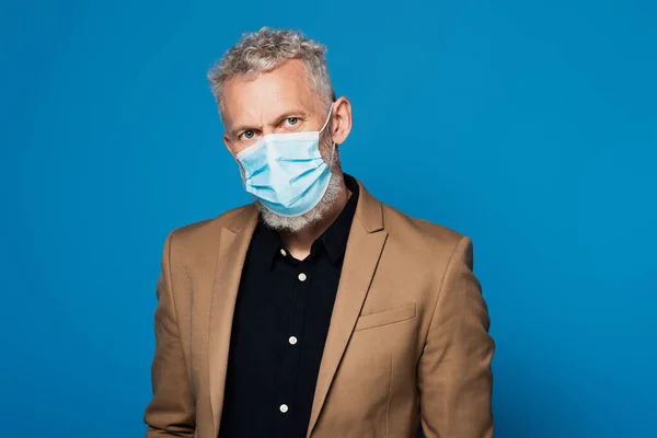 middle aged man in protective medical mask looking at camera isolated on blue