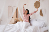 fiatal ázsiai nő selyem pizsamában ébred kinyújtott kézzel a hálószobában