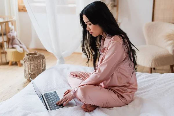 Concentrated Young Asian Woman Sitting Bed Crossed Legs Typing Laptop — Stock Photo, Image