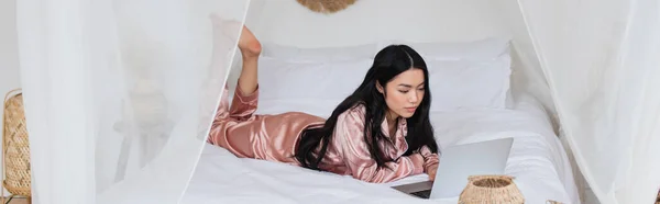 Молода Азіатка Шовковій Піжамі Лежить Ліжку Ноутбуком Сучасній Спальні Банер — стокове фото