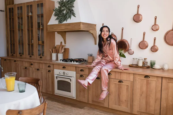 Young Asian Woman Pink Silk Pajamas Headphones Sitting Stove Kitchen — Stock Photo, Image
