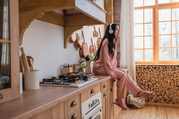 Glimlachende Jonge Aziatische Vrouw Roze Zijden Pyjama Koptelefoon Zitten Buurt — Stockfoto