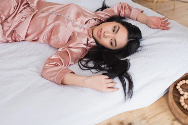 年轻的亚洲女人躺在白色的亚麻布上 伸出双手躺在卧室里的高角镜 — 图库照片