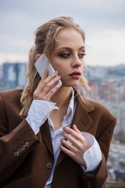 Dışarıda şık ceketli genç bir kadın akıllı telefondan konuşuyor. 