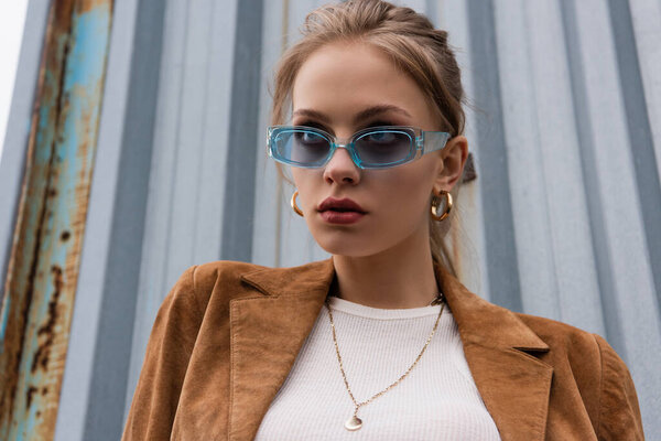 young woman in blue sunglasses and stylish jacket posing outside