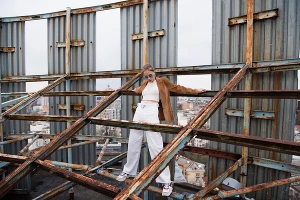 Moda kıyafetleri ve güneş gözlükleriyle çatıdaki yıpranmış yapının üzerinde duran genç bir model. 