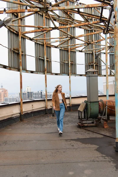 stock image full length of young woman in jeans and trendy sneakers walking on rooftop