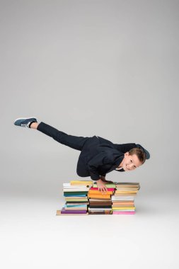 happy schoolboy doing handstand on pile of books on grey clipart