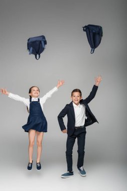 happy schoolkids throwing backpacks in air on grey clipart
