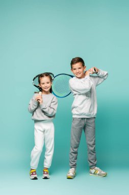happy kids in sportswear standing with tennis rackets on blue clipart