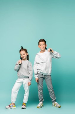 sportive children in sportswear standing with tennis rackets and smiling on blue clipart
