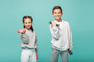 happy kids in sportswear working out with dumbbells isolated on blue clipart