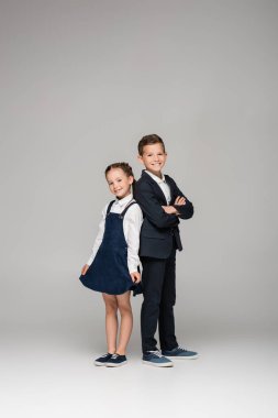 happy schoolboy standing with crossed arms near girl in dress on grey clipart