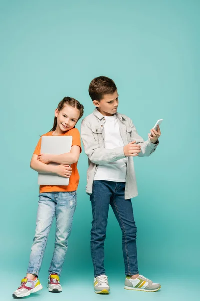 Счастливая Девочка Ноутбуком Стоящая Рядом Мальчиком Используя Смартфон Голубом — стоковое фото