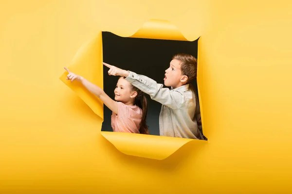 Çocuklar Sarı Arka Plandaki Delikten Parmaklarını Göstererek Uzaklaşıyor — Stok fotoğraf
