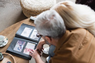 Overhead view of blurred elderly couple sitting near photos in album on table 