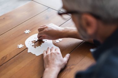 Blurred man with dementia folding jigsaw on table at home  clipart